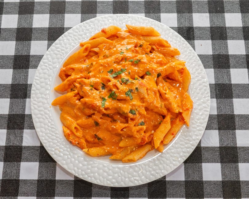 Penne pasta in a creamy tomato sauce, garnished with fresh herbs, on a white plate.