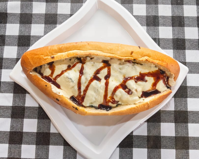 A long, golden-brown bread filled with melted cheese and drizzled with a dark sauce on a white plate.