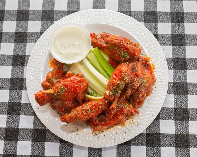Spicy buffalo wings with celery sticks and a side of ranch dressing on a white plate.