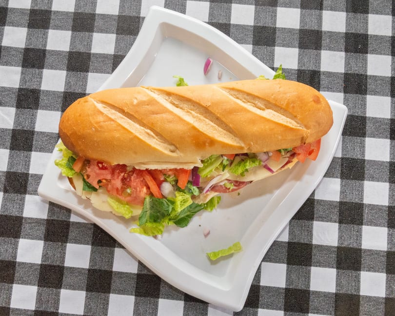 A large submarine sandwich with lettuce, tomato, onion, cheese, and deli meat on a white plate.