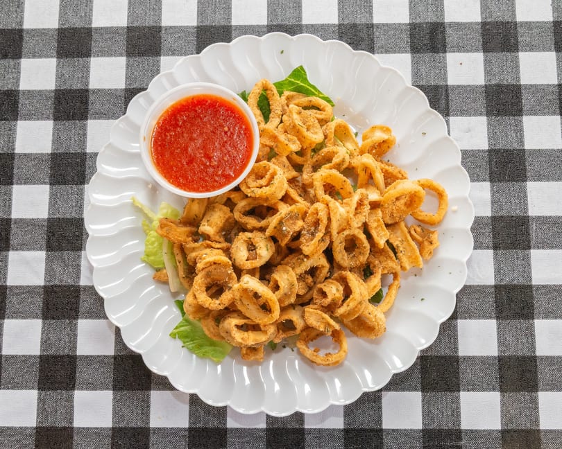 Crispy fried calamari rings with a side of red marinara sauce on a white scalloped plate.