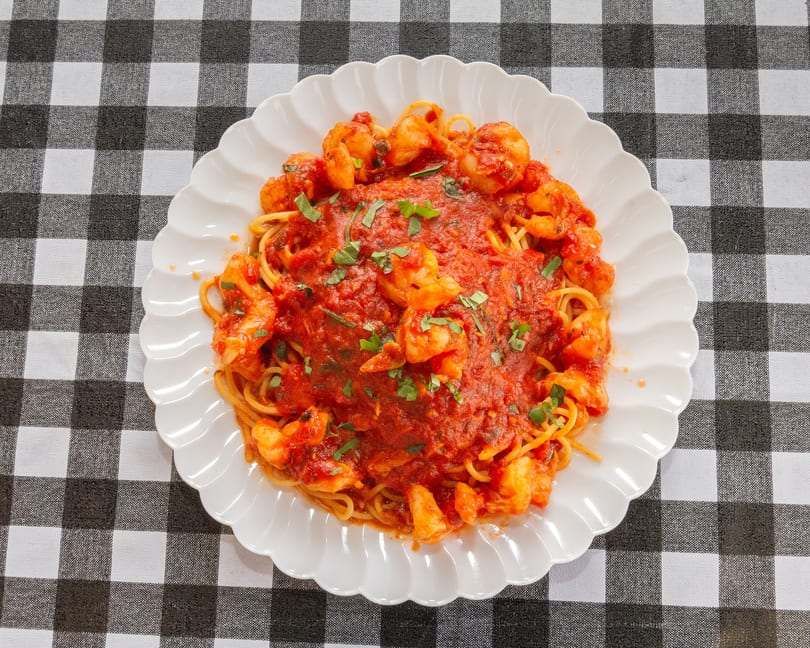 Spaghetti with shrimp and red sauce, garnished with basil, on a white plate over a checkered tablecloth.